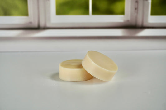 Two zero-waste solid conditioner bars with a creamy white color, shown on a white surface against a window background.