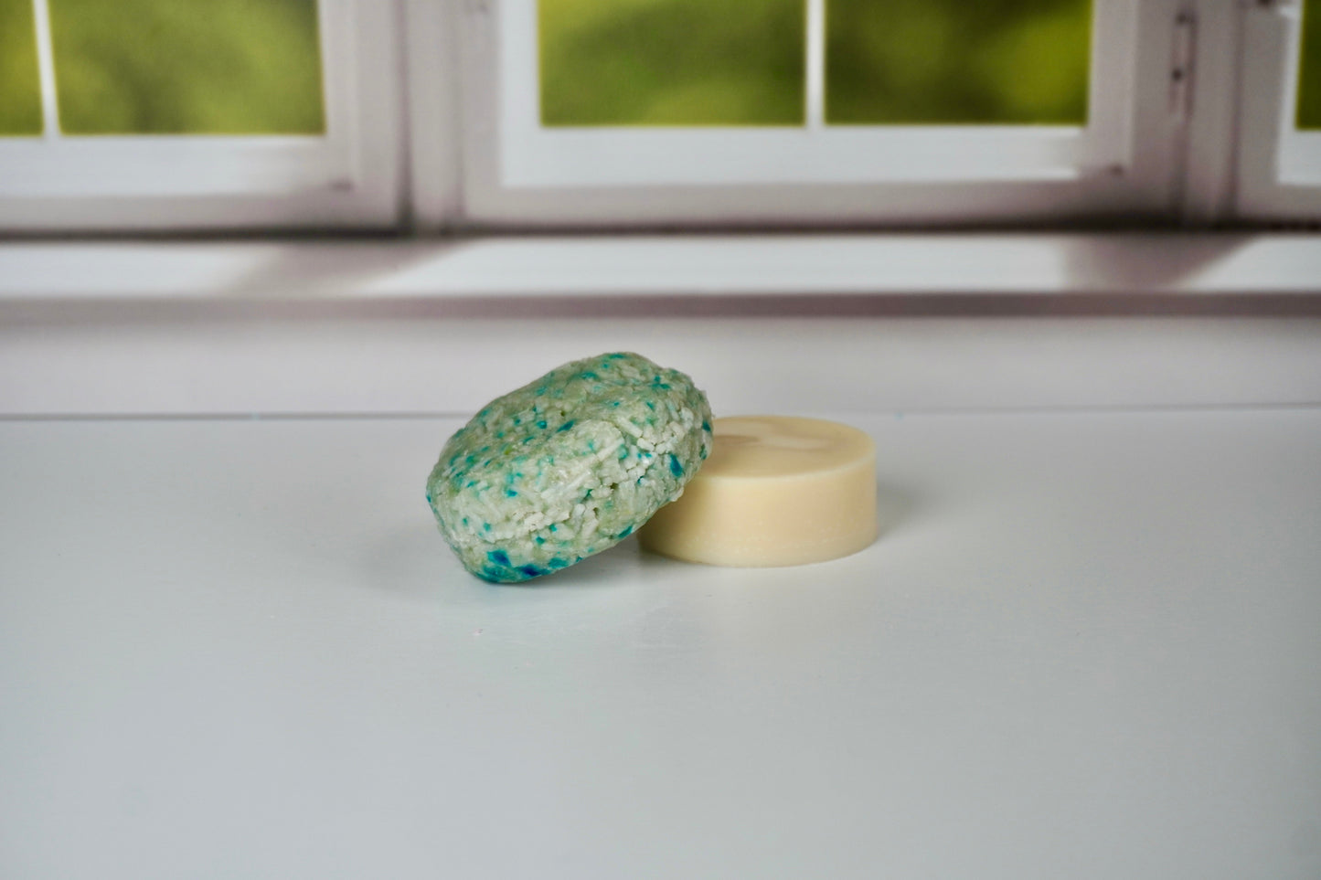 Detox shampoo bar and conditioner bars sitting on a white table with a window in the background