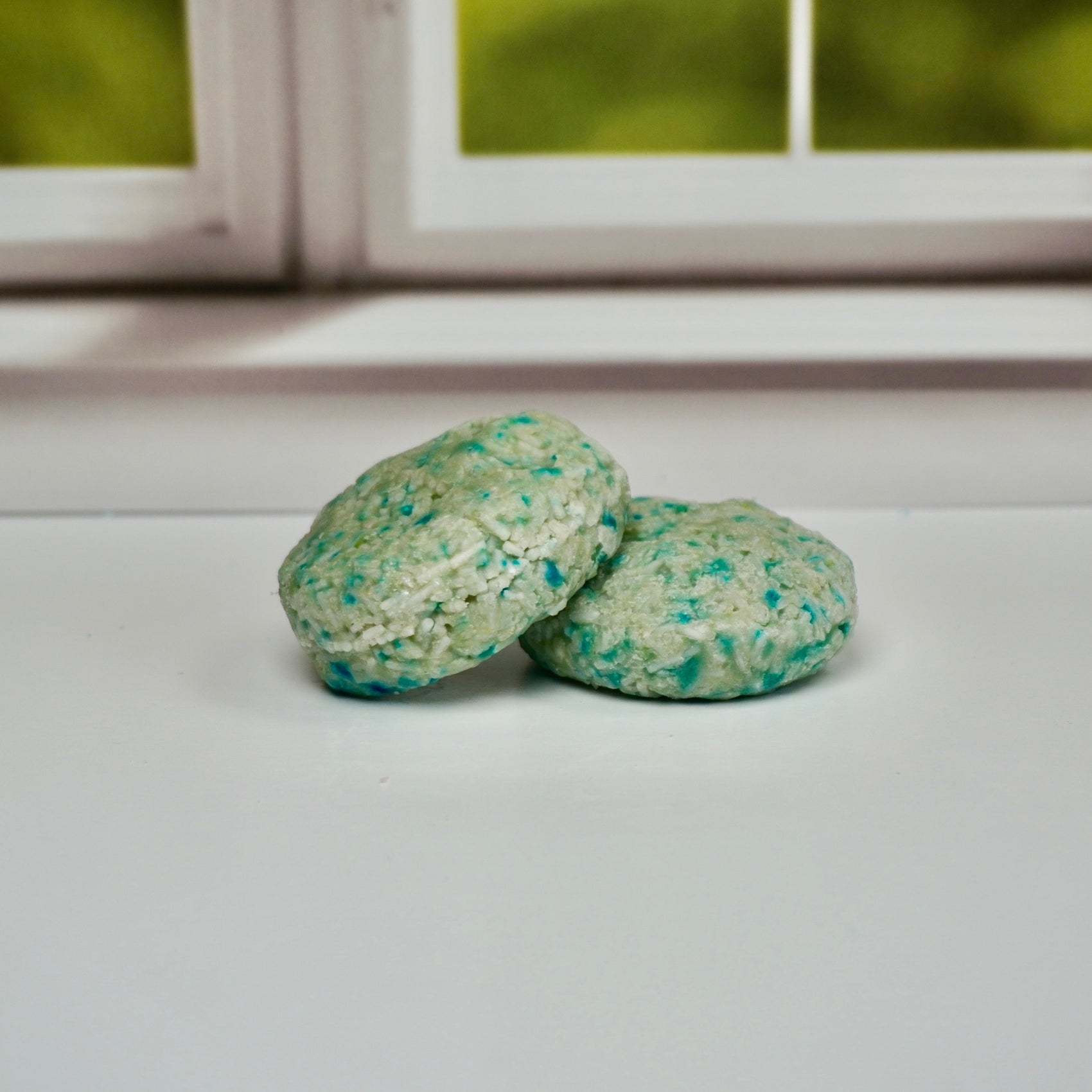 Two shampoo bars on a white surface with a window in the background