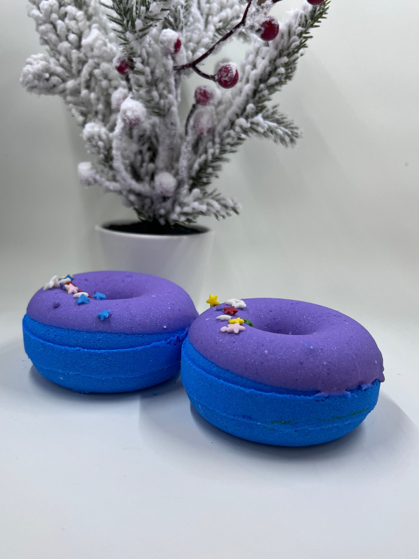 two Blue frosted donut baths bombs stting in front of a small pine tree