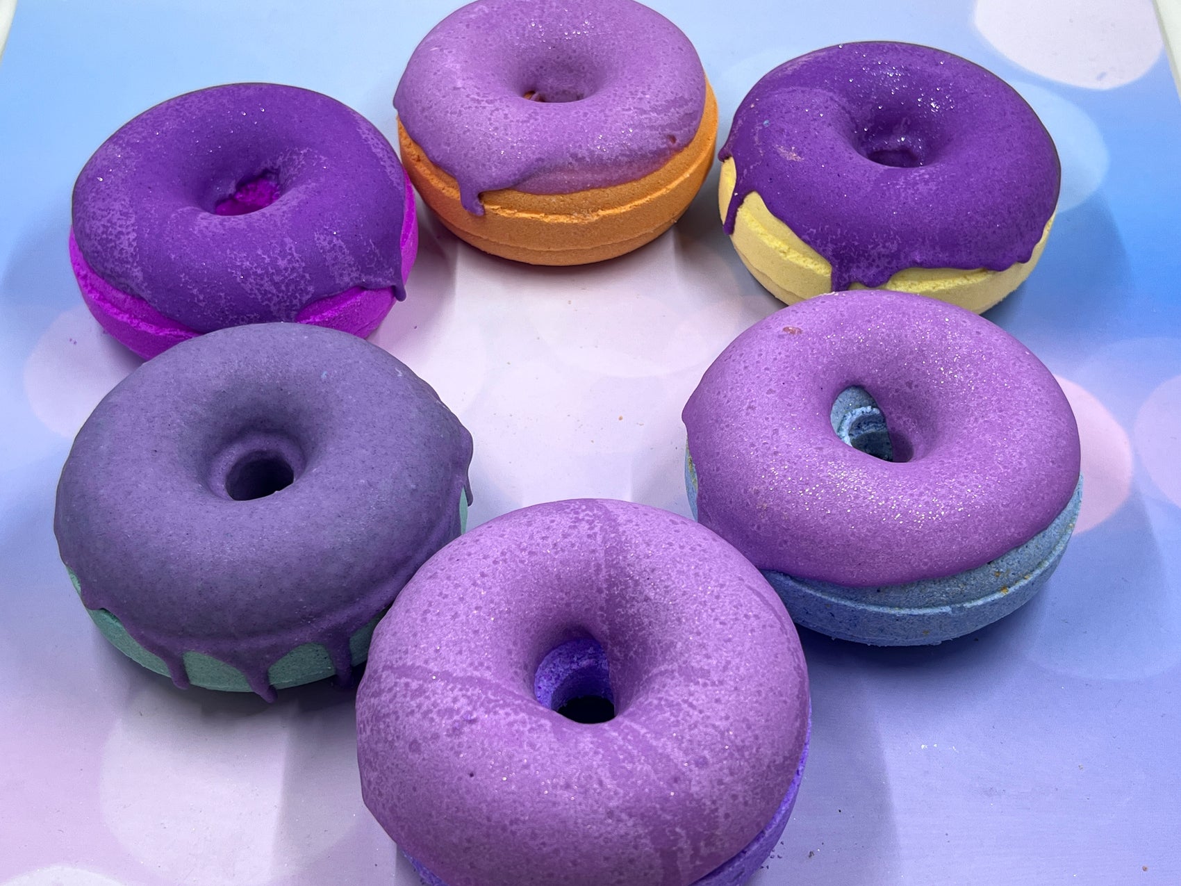 Donut-shaped bath bombs arranged in a circle, featuring rainbow and purple frosting