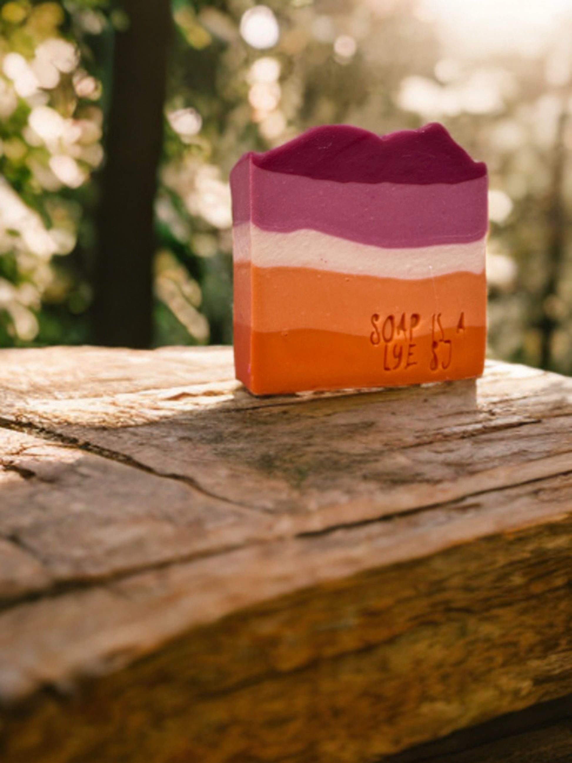 Three-layered soap bar with 'Soap is a Lye' text on a wooden surface outdoors