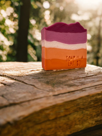 Three-layered soap bar with 'Soap is a Lye' text on a wooden surface outdoors