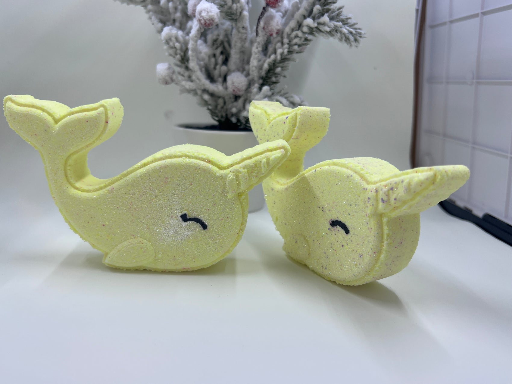 yellow narwhal bath bombs in front of a holiday tree and they are smiling