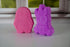 Pink and purple penguin and unicorn bath bombs on a white surface with a blurred background