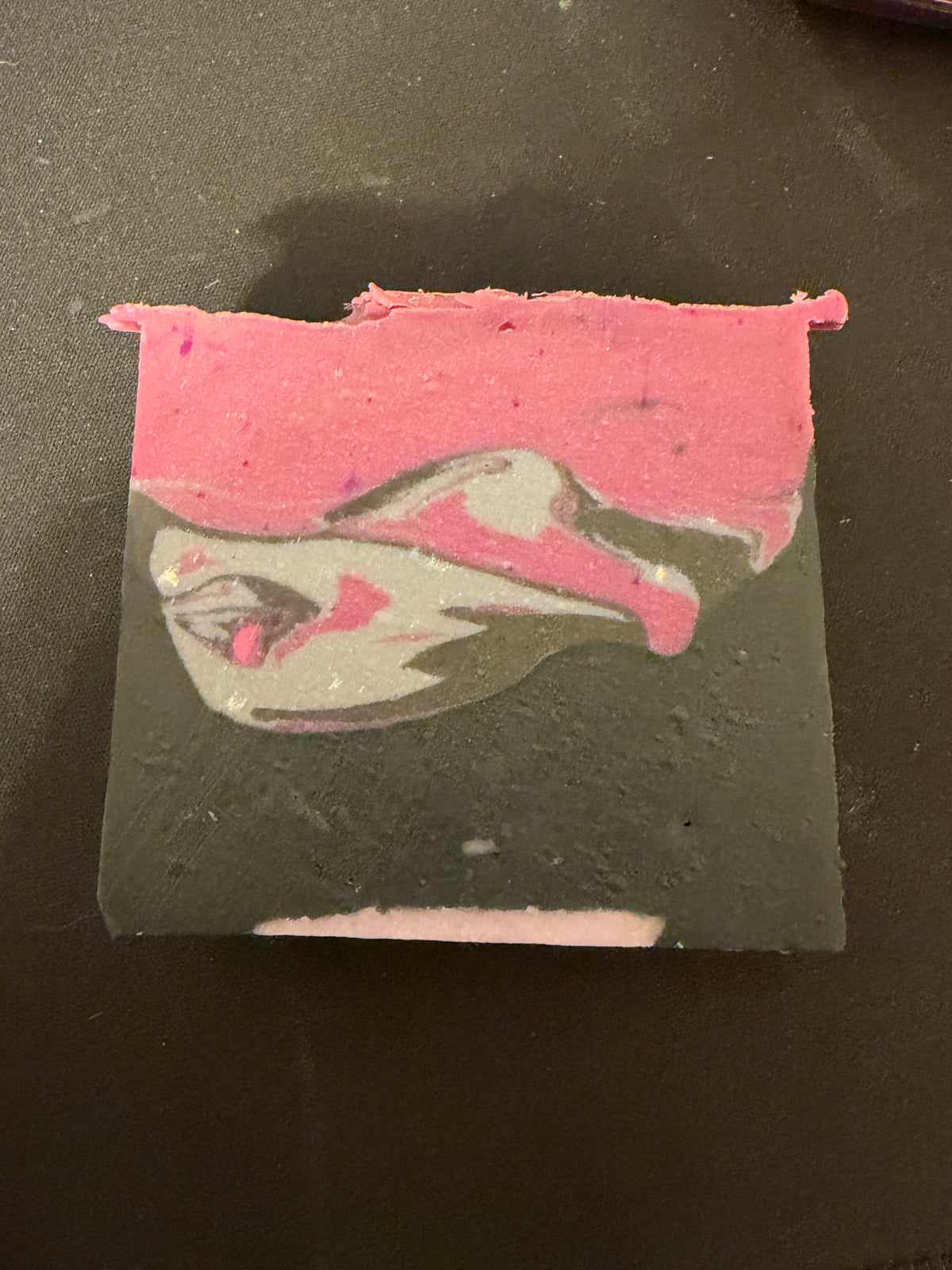 A rectangular bar of soap with a swirled pattern of pink, dark gray, and white, resting on a dark surface.