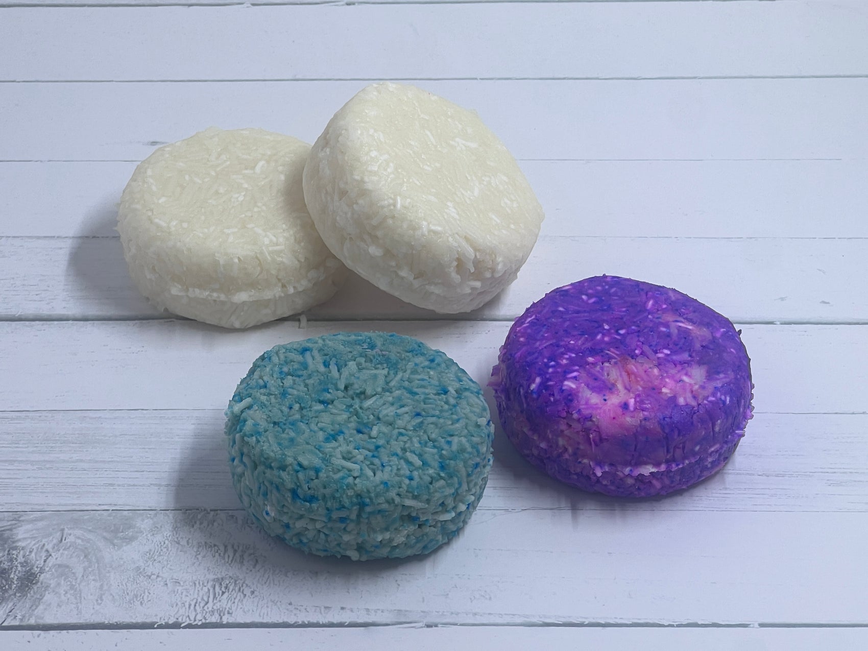 Multiple shampoo bars sitting next to each other one is purple, one is green, and two are white
