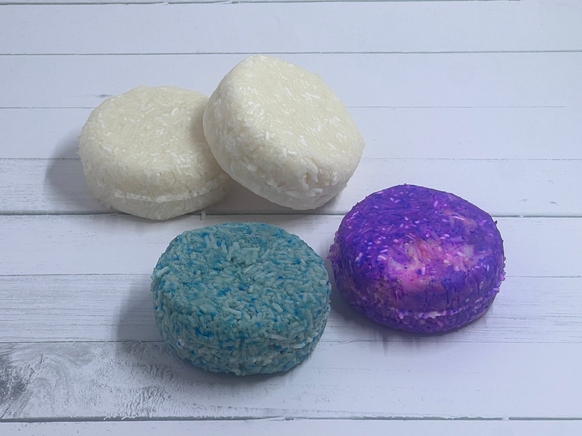 Multiple shampoo bars sitting next to each other one is purple, one is green, and two are white