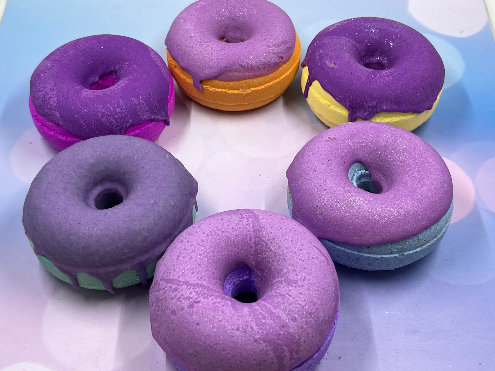 rainbow bath bombs in a circle shaped as donuts with purple frosting